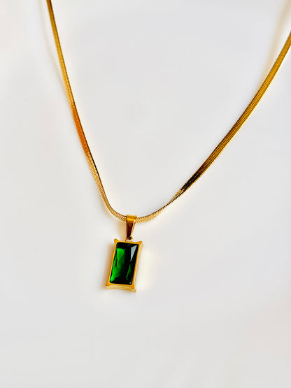 Gold necklace with a green gemstone pendant on a white background